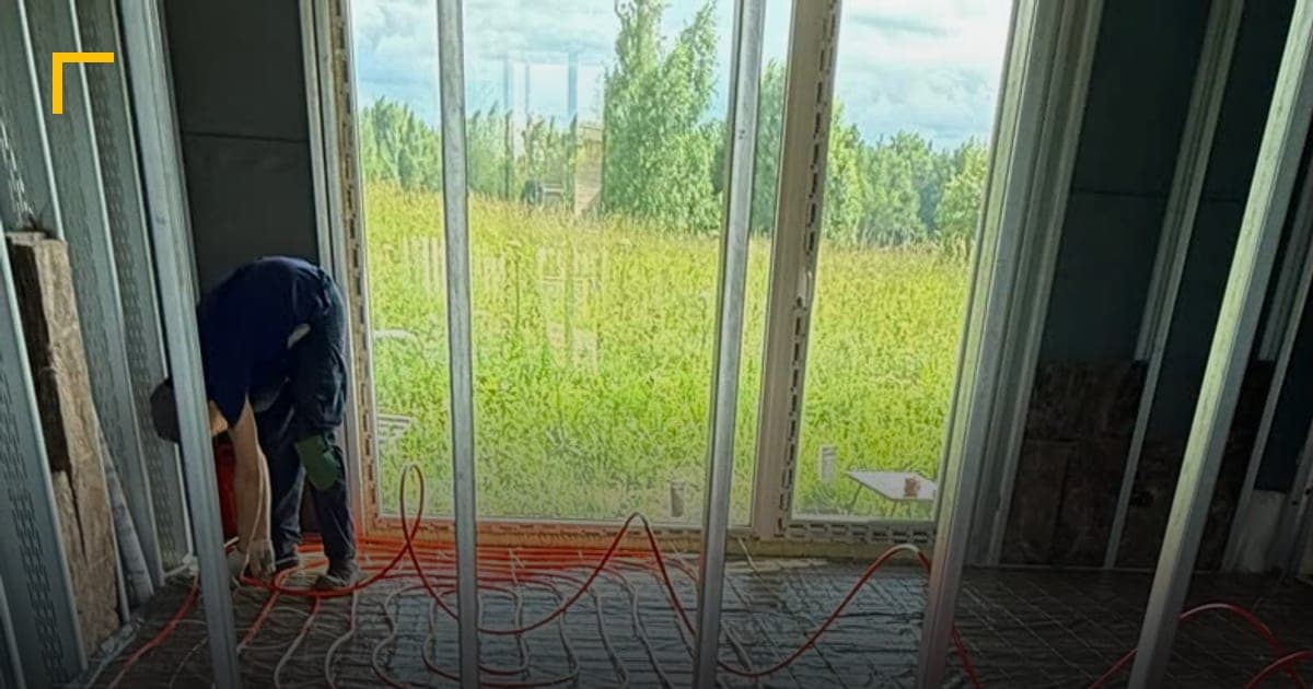 Красная труба водяного тёплого пола уложена улиткой и закреплена хомутами к сетке в комнате дома из ЛСТК с панорамным окном